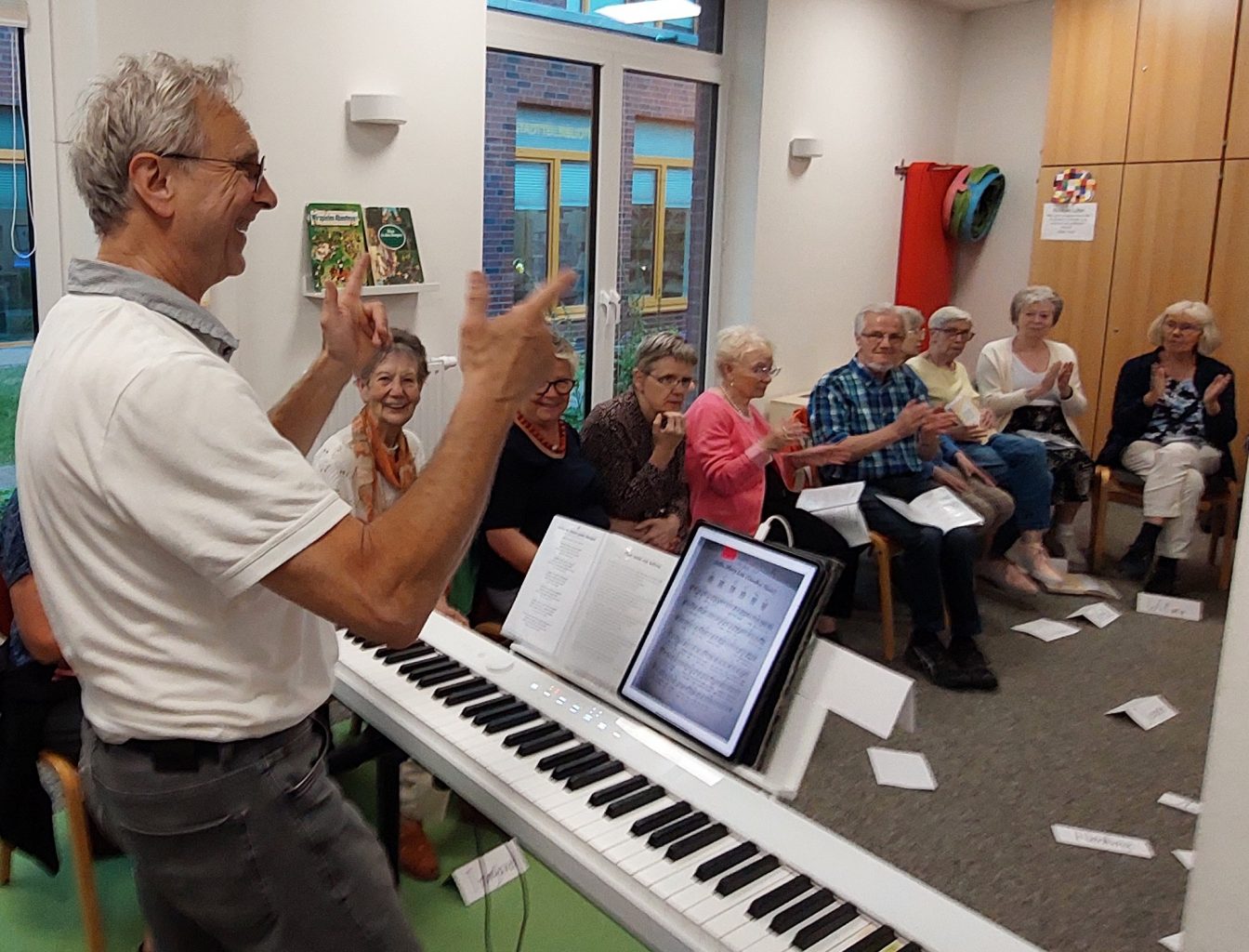 Mann steht dirigierend am Keyboard und leitet eine Gruppe Senior*innen an, die am Projekt 