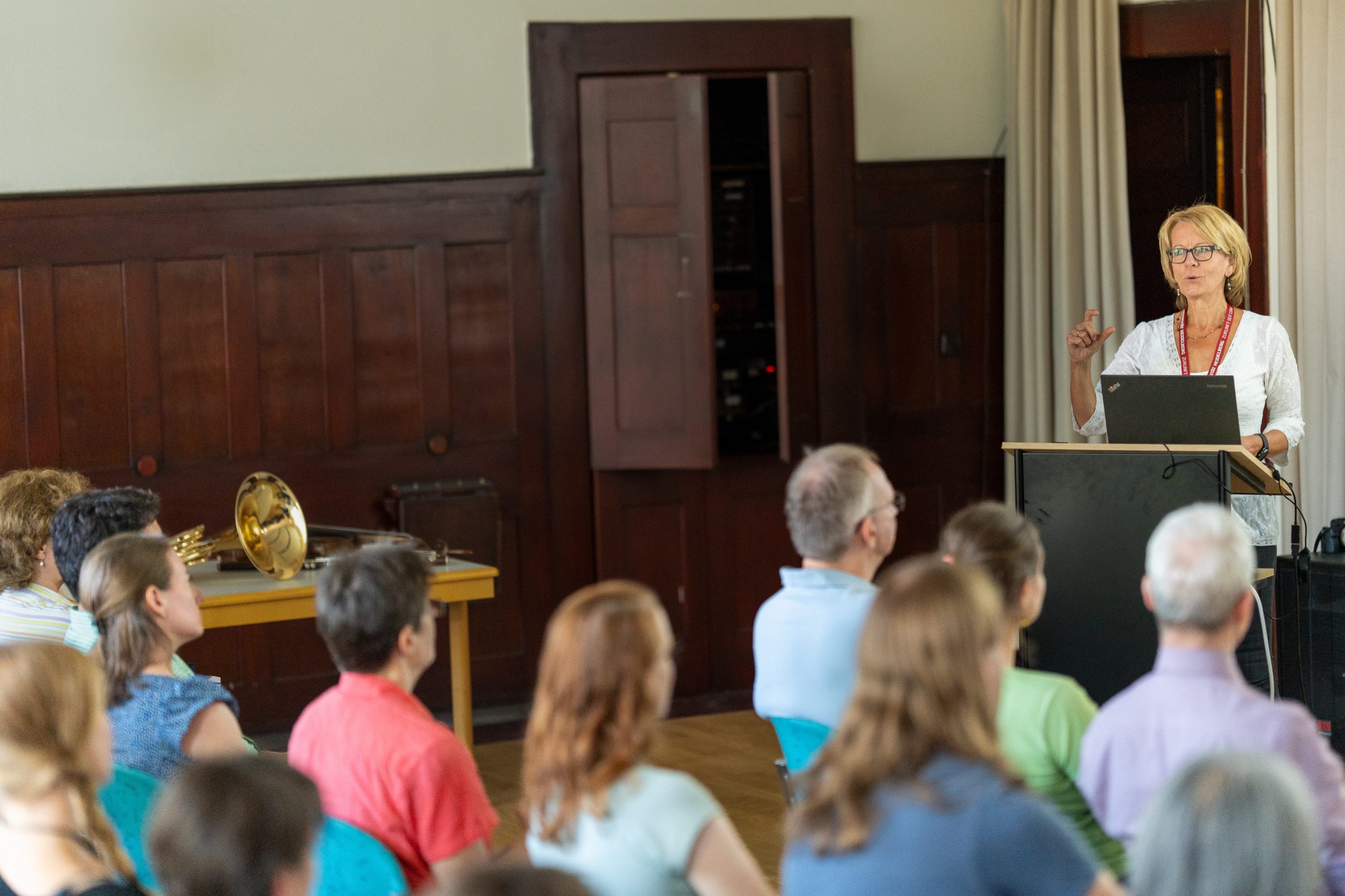 Ein Publikum hört einer Frau zu, die hinter einem Pult steht.
