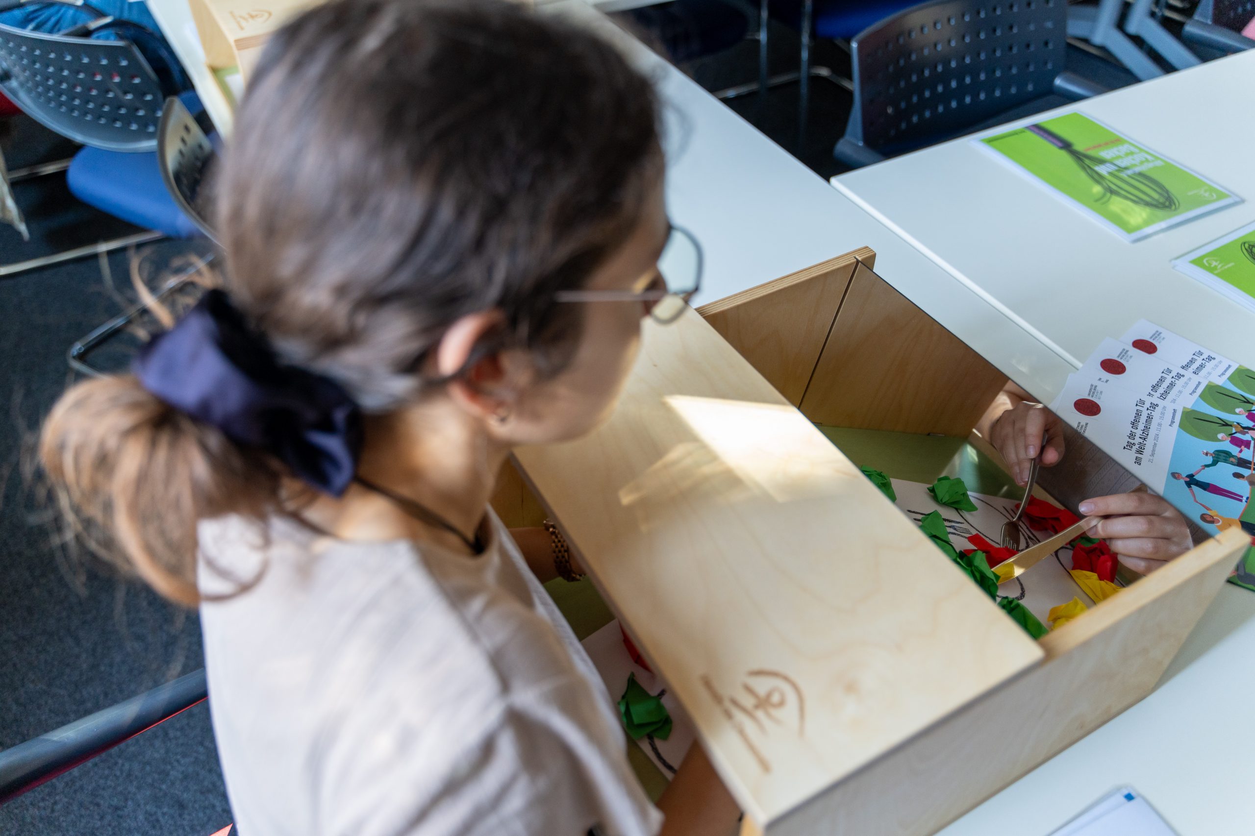 Eine Frau beugt sich über eine Box des Demenz Simulators