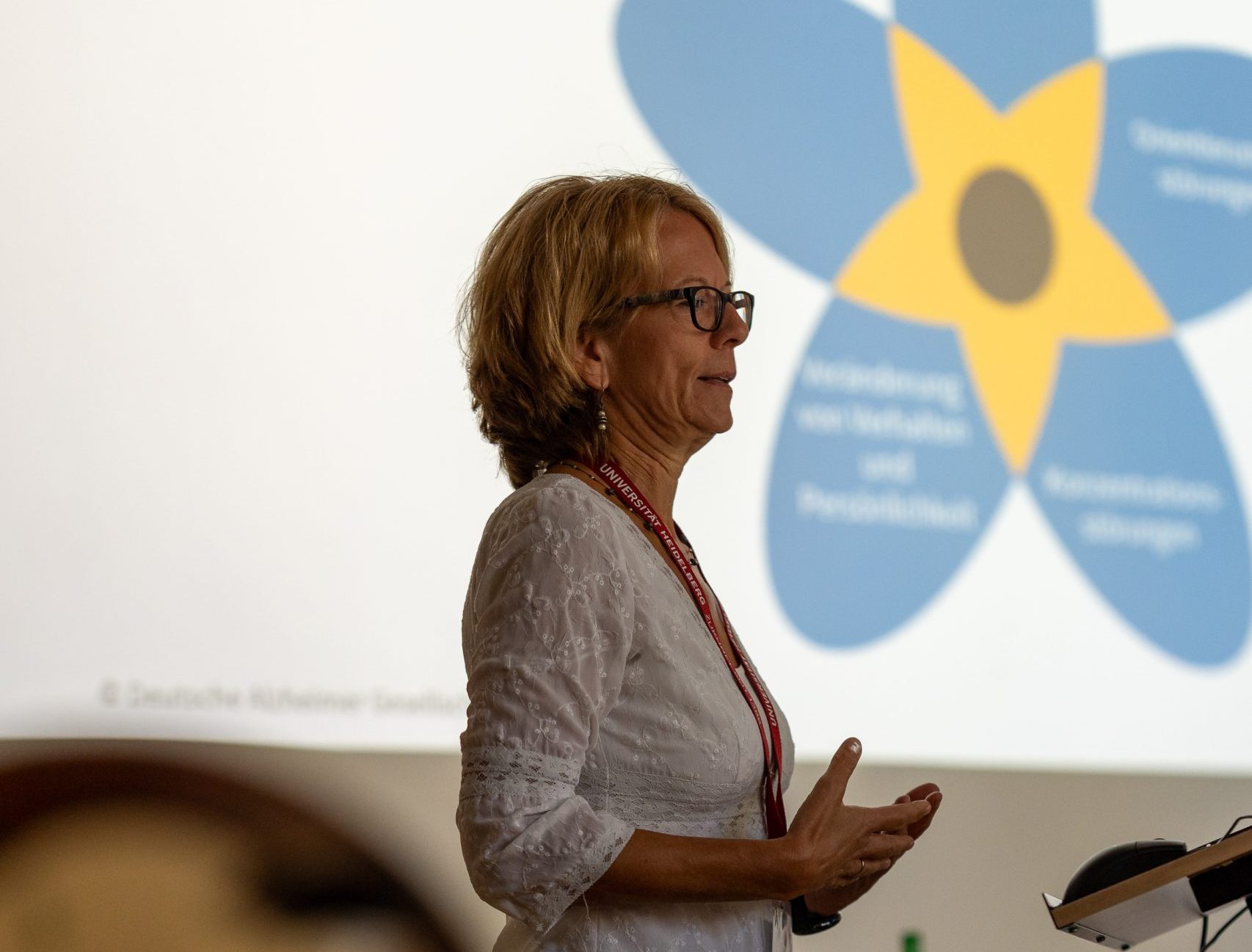 Frau steht sprechend vor einer Leinwand. Davor liegt unscharf ein Horn.