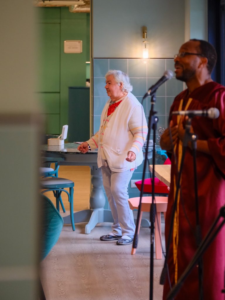 Im Vordergrund singt ein Gospelchor. Im Hintergrund ist eine Seniorin aufgestanden, um zur Musik zu tanzen.