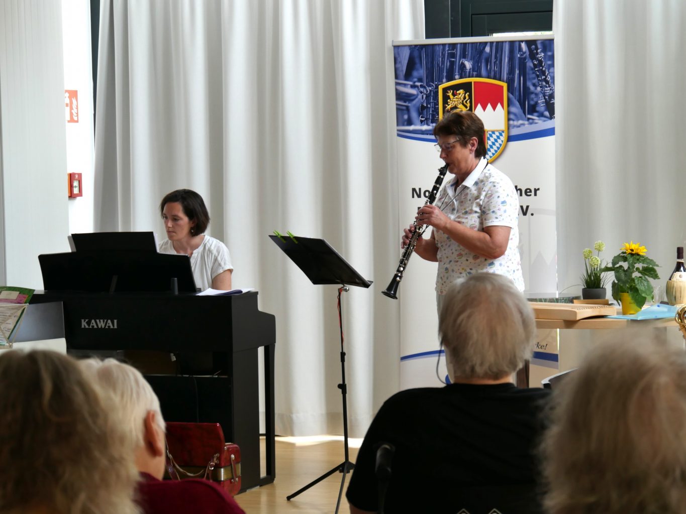 EIne Klarinettenspielerin und eine Klavierspielerin musizieren vor Senior*innen. 