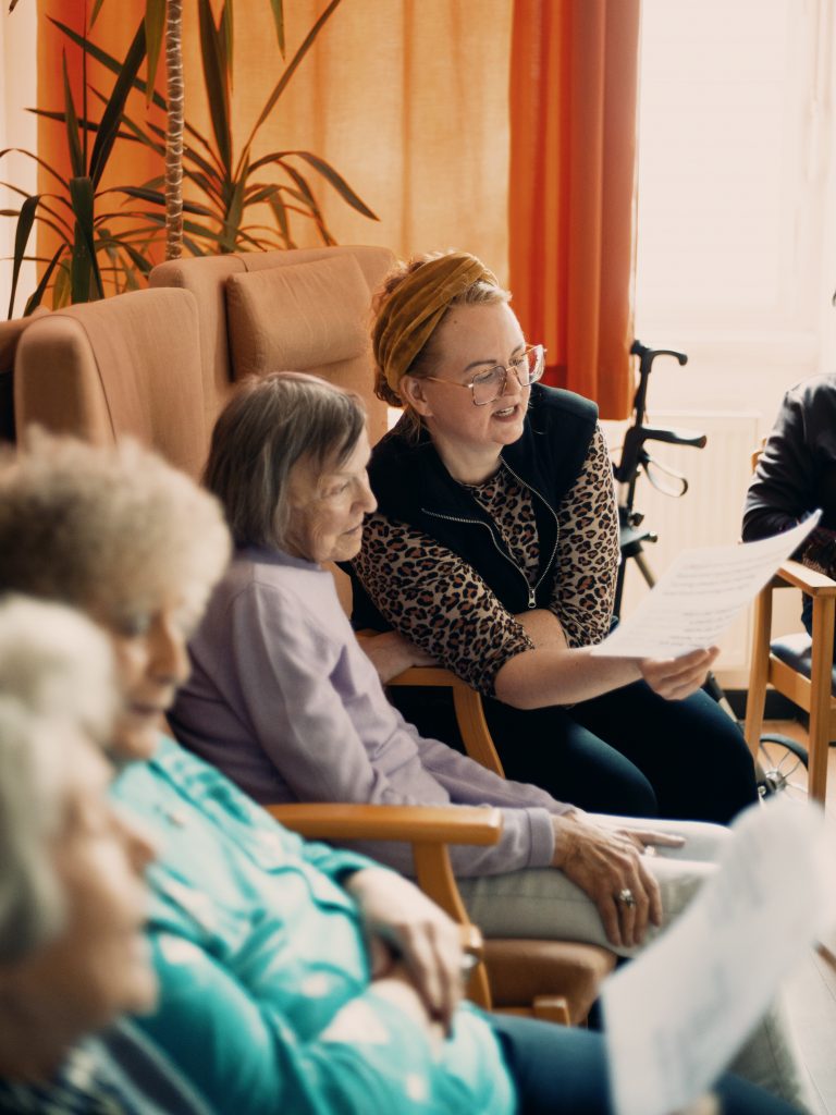 Eine Mitarbeiterin sitzt bei einer älteren Frau. Gemeinsam singen sie vom Blatt. 