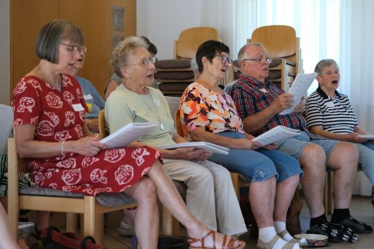 Fünf Senior*innen sitzen in einer Reihe und singen angeregt. 