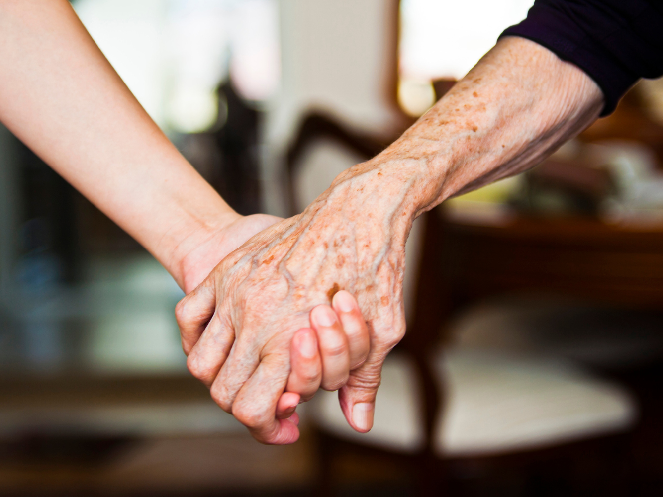 Zwei Menschen halten sich die Hand - eine jung, eine alt. 