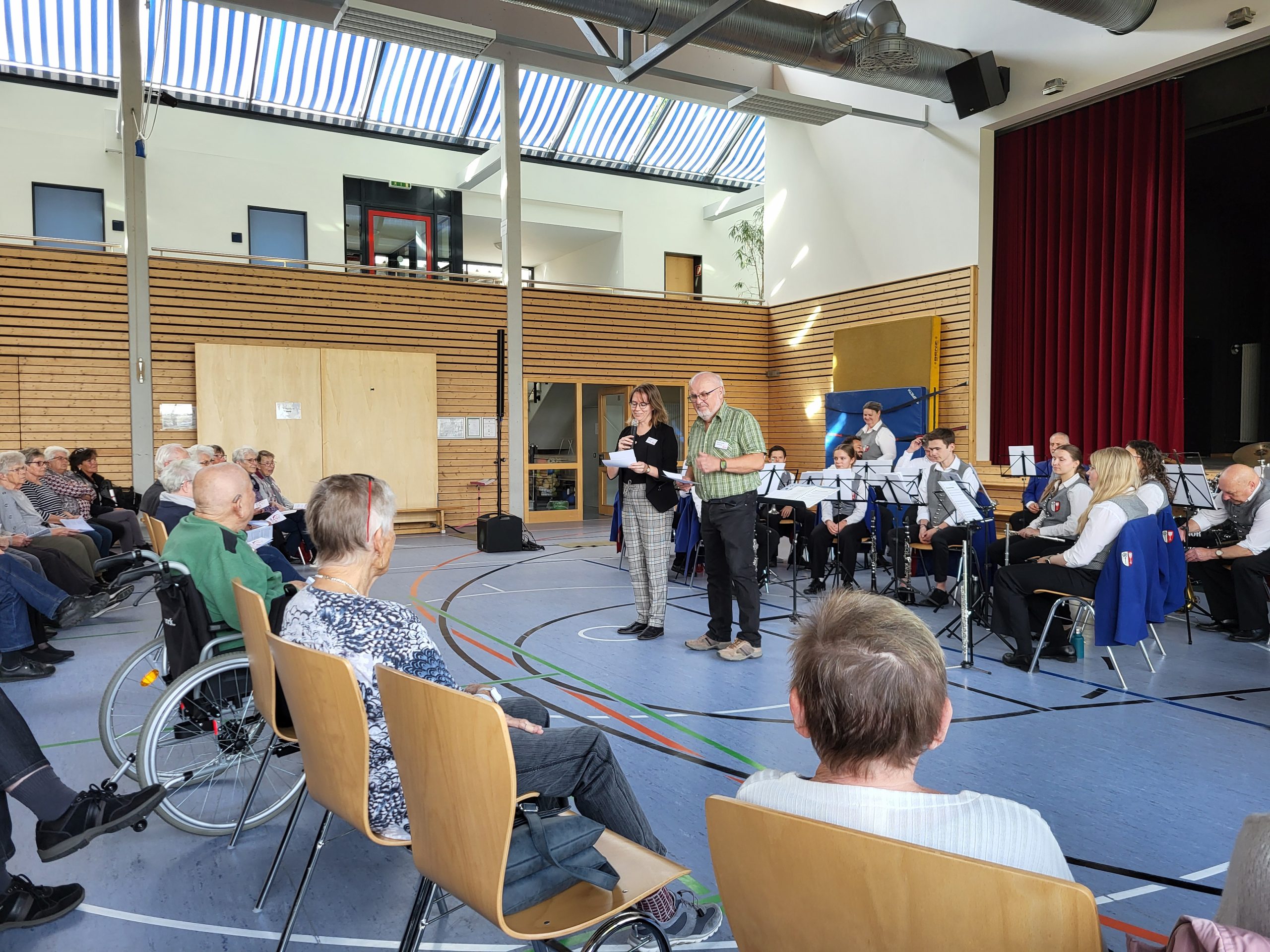 Senior*innen sitzen auf Stuhlreihen, vor ihnen ein Bläserensemble.