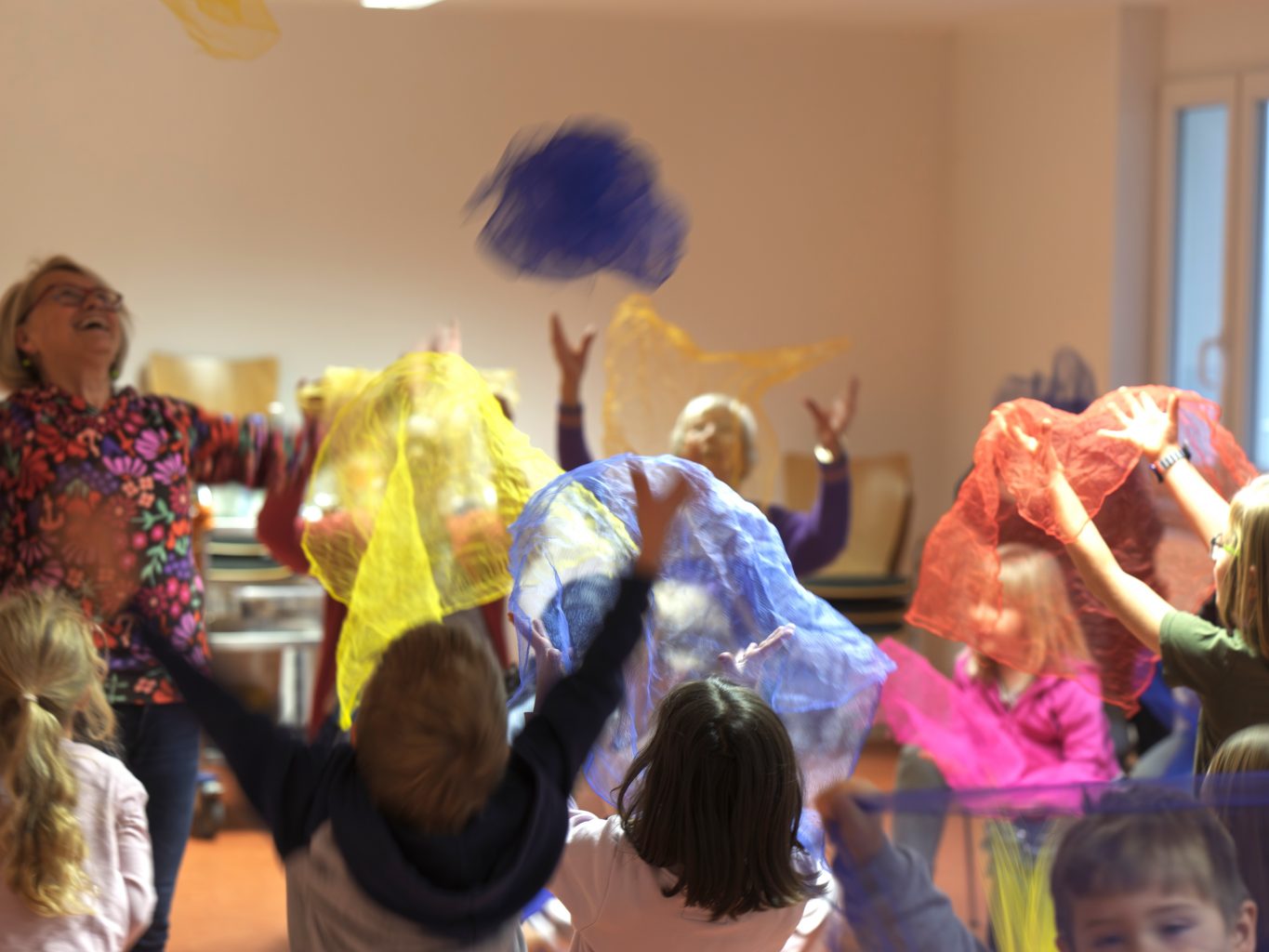 Kinder tanzen mit bunten Tüchern und haben sichtlich viel Freude. 