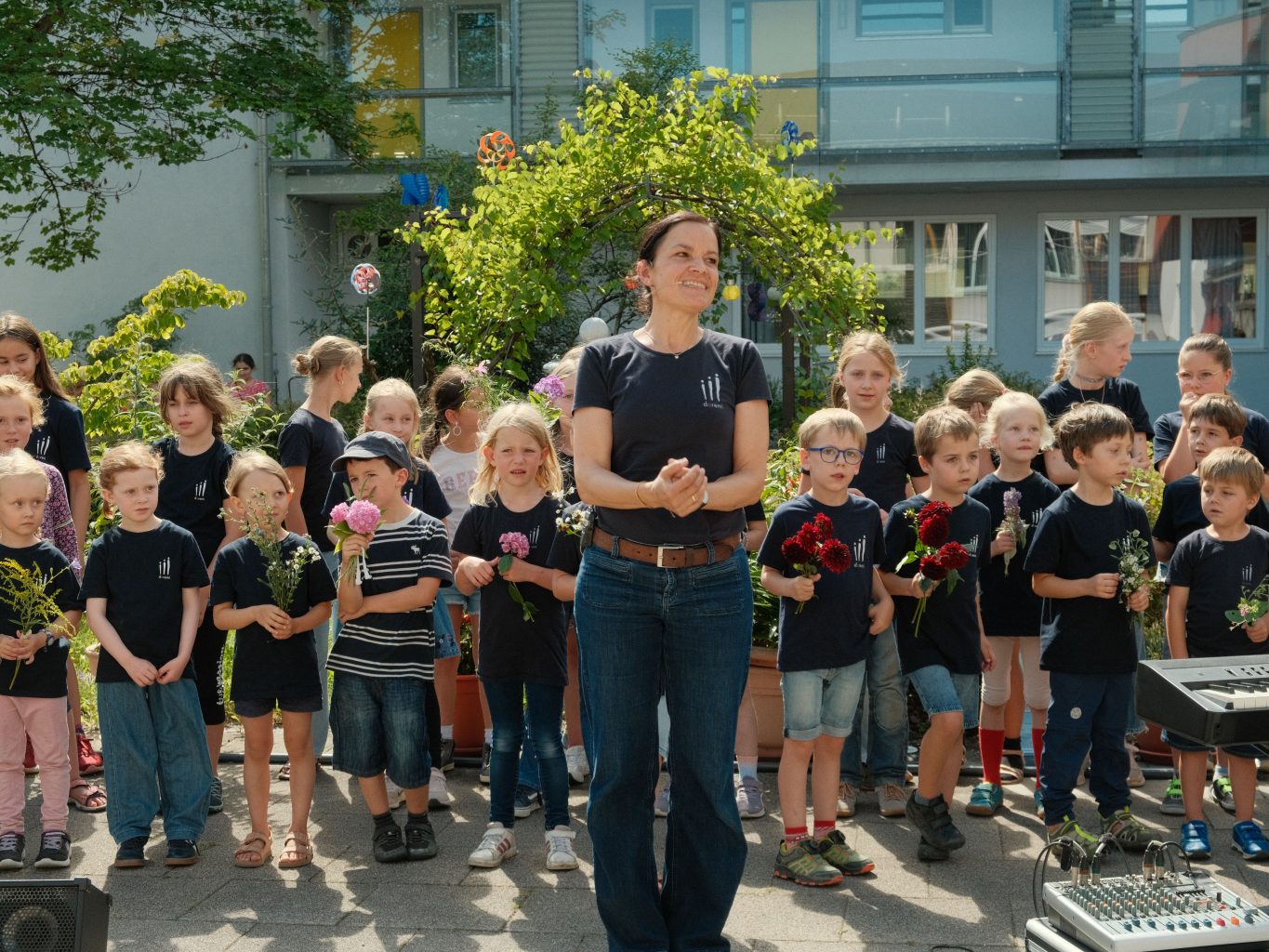 Die Projektleitug spricht, hinter ihr stehen Kinder mit Wiesenblumensträußen.