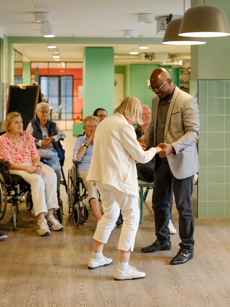 Ein Projektmitarbeiter und eine Seniorin tanzen gemeinsam. 