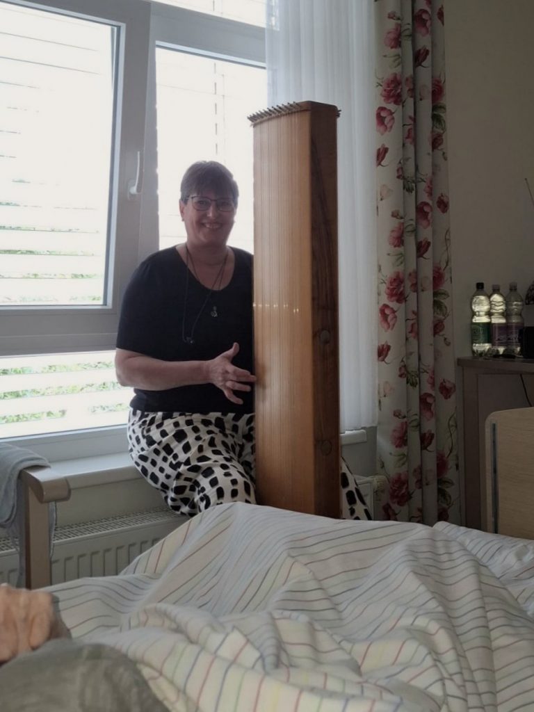 Harfenspielerin spielt am Bett einer älteren Person. 