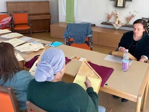 Drei Frauen sitzen am Tisch und spielen Tischharfe. 