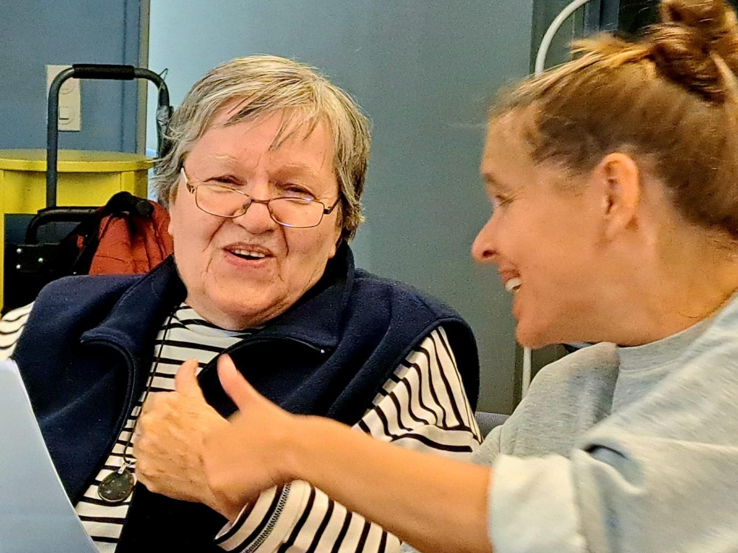 Eine Seniorin und eine Betreuerin schauen in ein Liedblatt, lachen und halten die Daumen hoch.