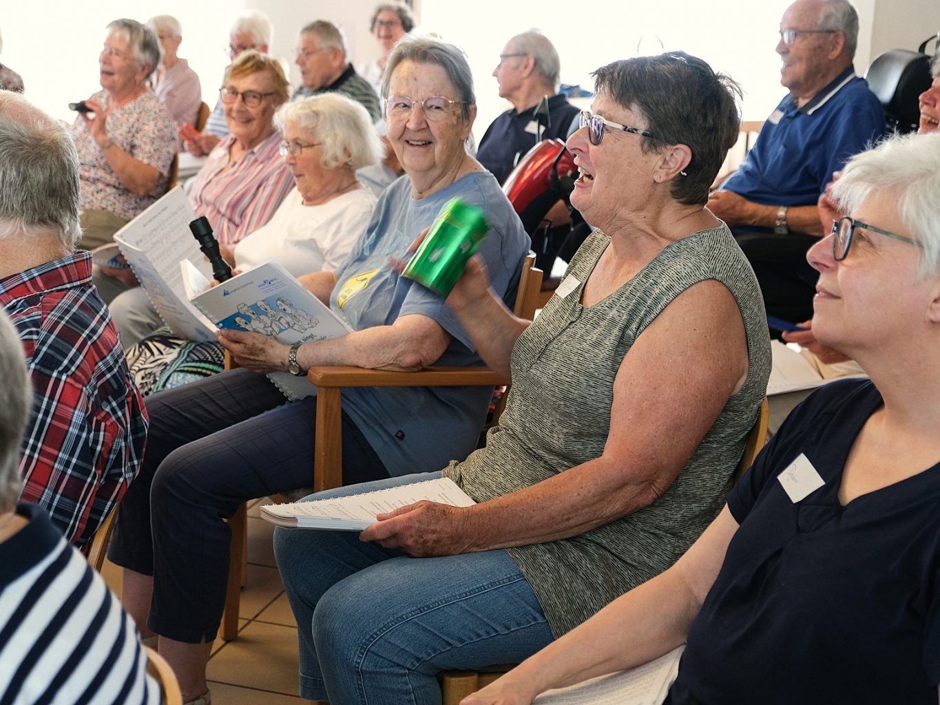 Senior*innen sitzen und singen gemeinsam. Manche haben Rasseln in der Hand. Sie lächeln, lachen und blicken sich an. 