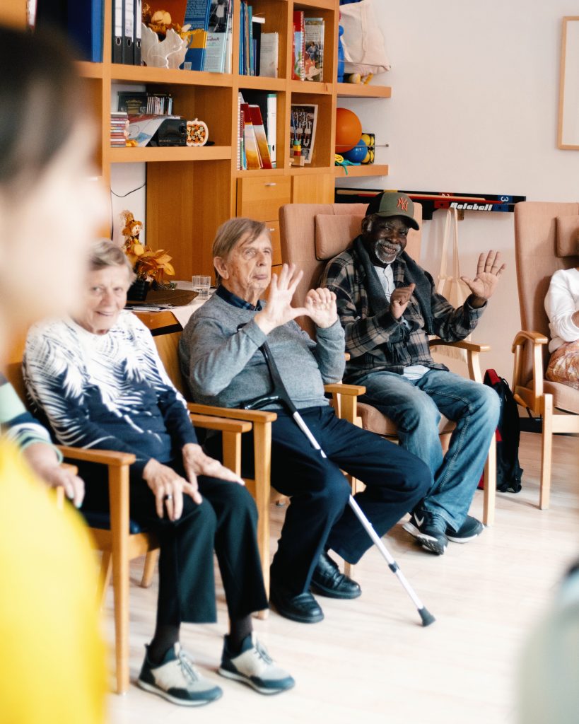 Senior*innen sitzen im Kreis und bewegen gemeinsam die Hände zu Musik. 