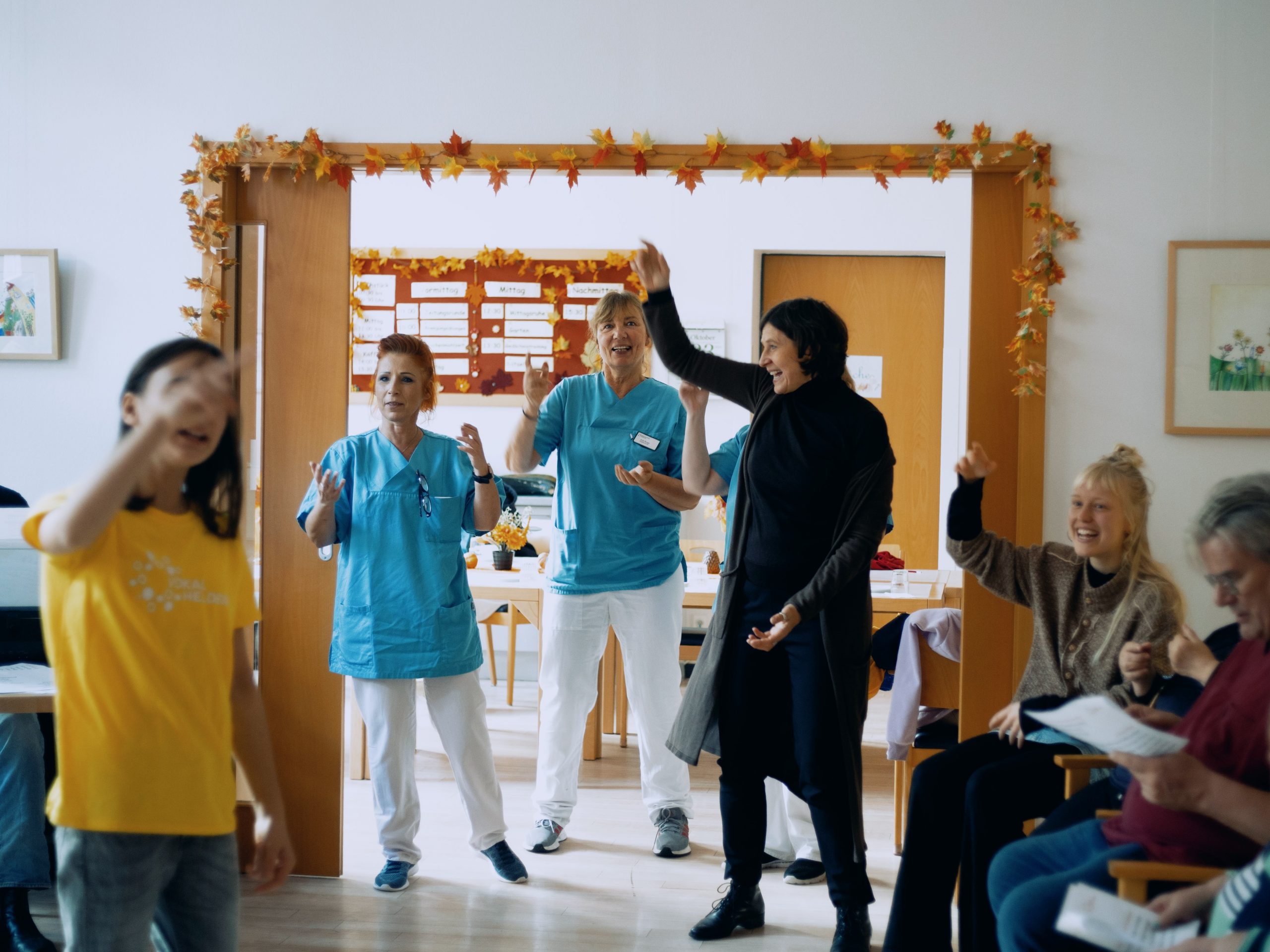 Die Projektleitung und Pflegekräfte führen gemeinsam Bewebungen vor. SIe lachen herzlich.