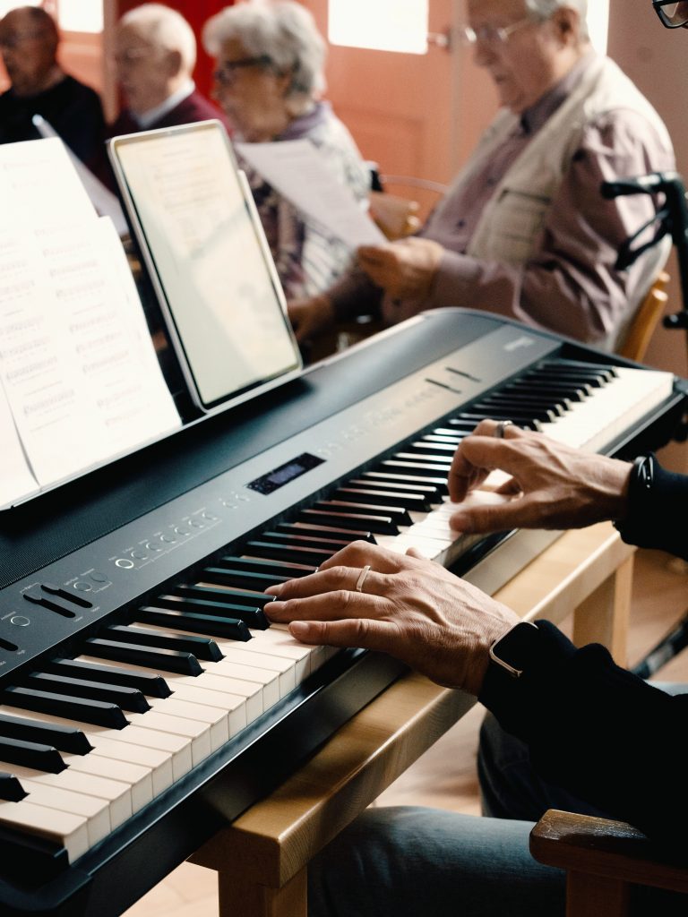 Eine Person spielt am Keyboard, im Hintergrund sitzen Senior*innen und singen gemeinsam. 